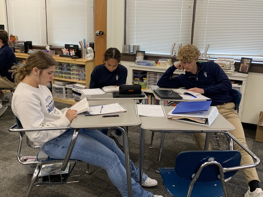 A group of 8th graders read a passage together from their book before discussing.